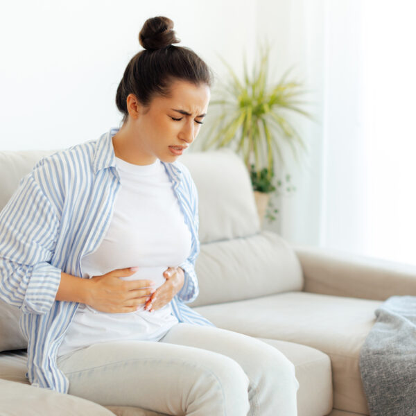 Sad arabian or indian woman sitting on a sofa, suffering stomach ache, constipation, cramp, nausea or bloated, holds her stomach with her hands, stomach pain, problems with indigestion, menstruation
