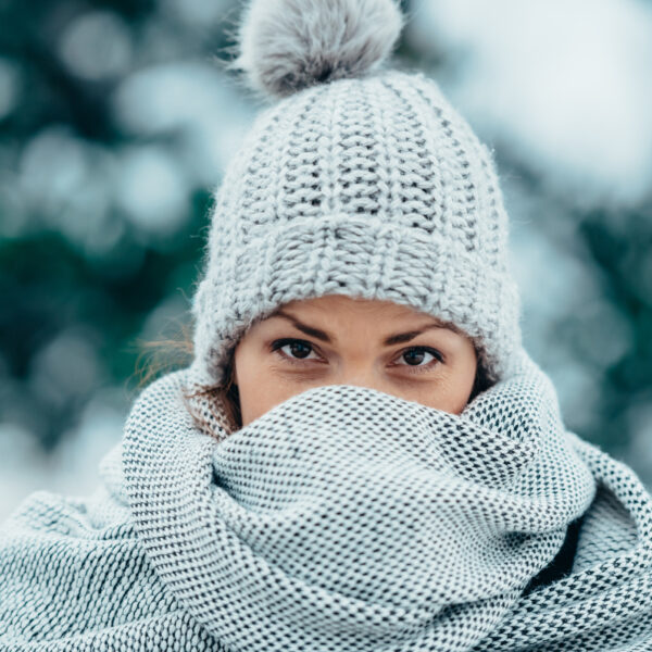 Portrait of a beautiful young woman wearing scarf and a a hat on a cold winter day during snow