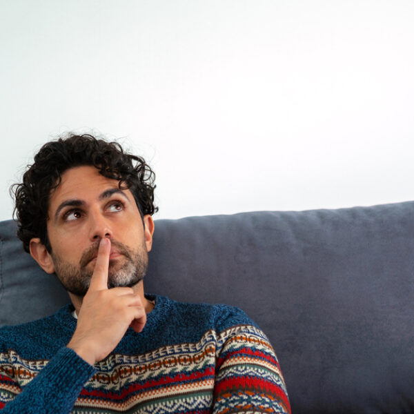 Face of thoughtful adult man looking up pensive while sitting on couch home. Bearded man making choice or thinking on a sofa looking away. A person over white background